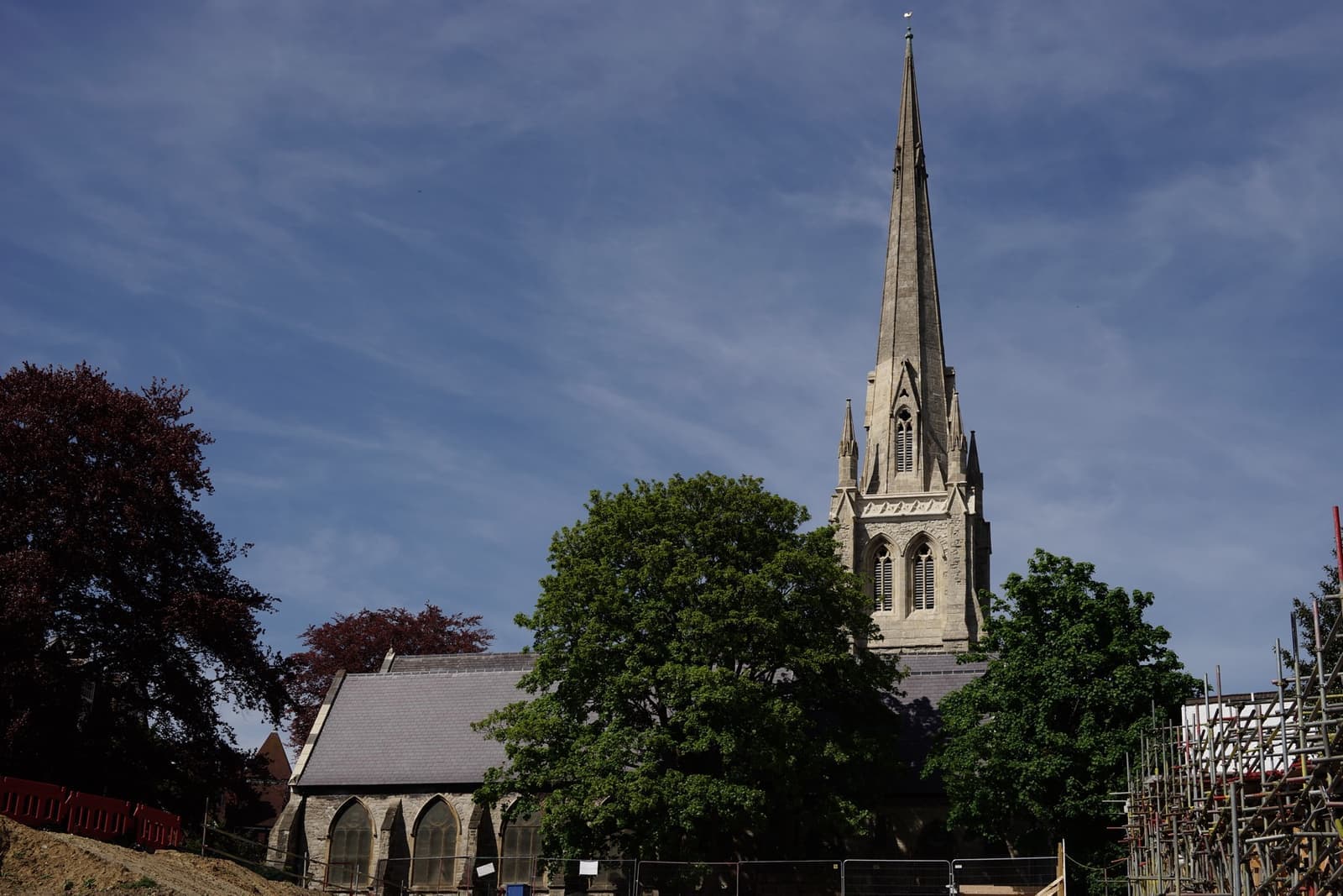 A Victorian church with a tall stone spire among trees