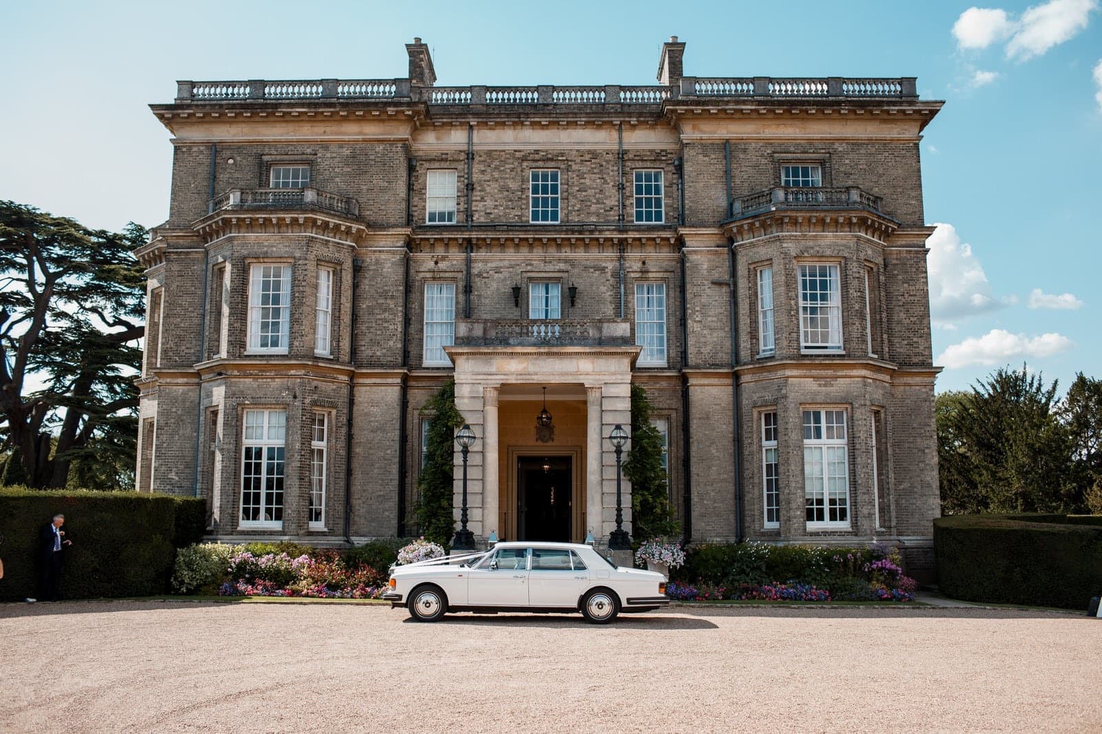 A pale Victorian country house with a wedding car parked outside