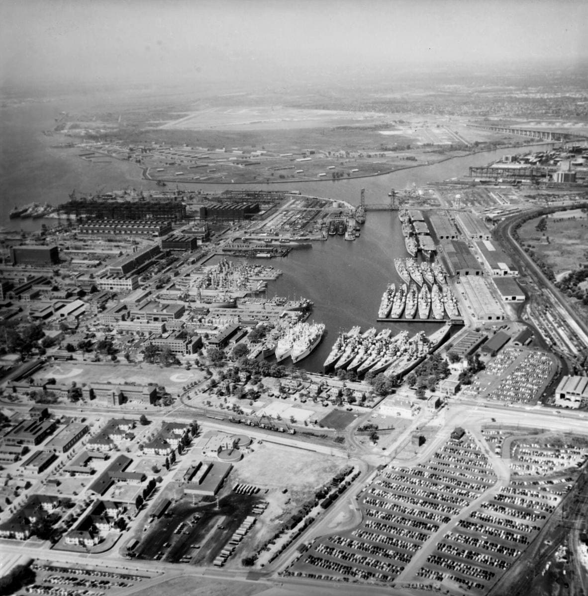 Aerial view of a naval dockyard with rows of grey warships moored in a basin