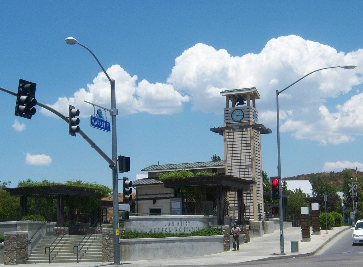 A suburban rail platform under a clear sky with low hills behind
