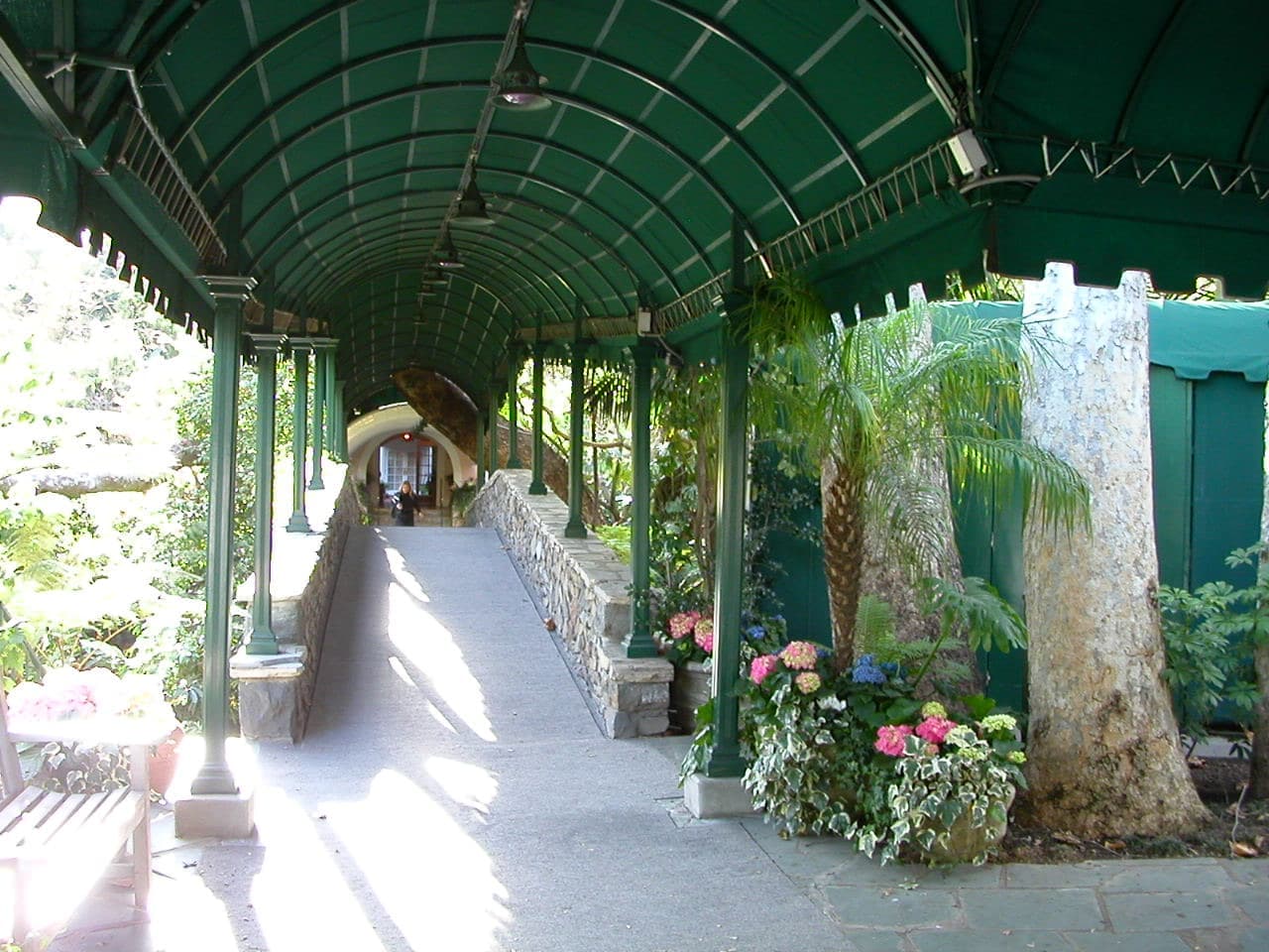 A shaded, flower-lined entrance path to a pink mission-style hotel