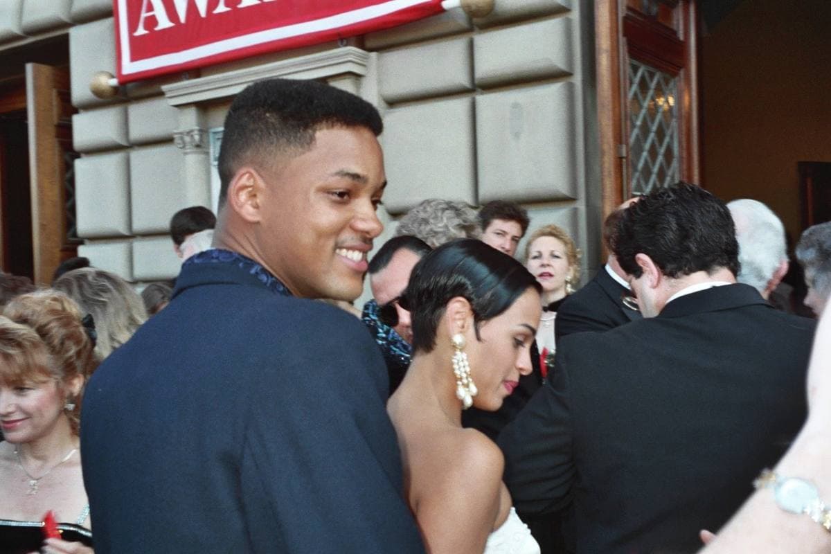 Will Smith smiling outside a stone building, in a dark jacket