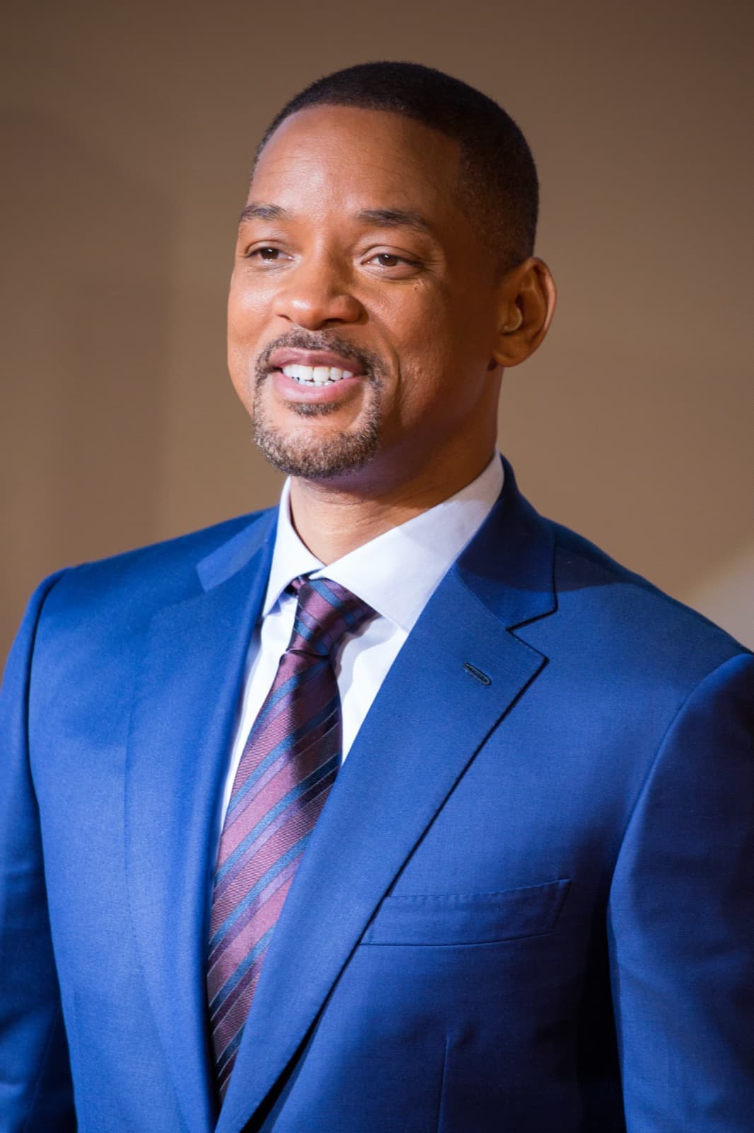 Will Smith smiling on a red carpet in a dark jacket