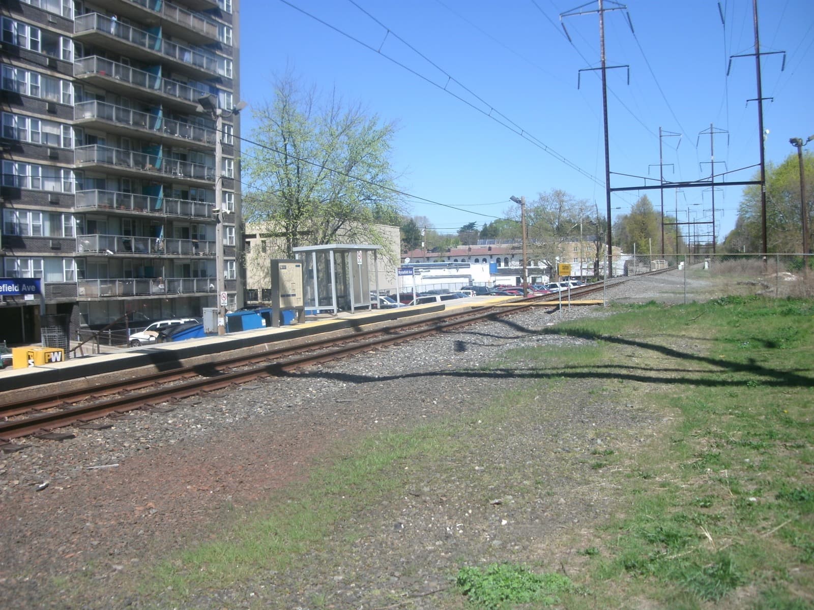 A small suburban railway platform with a shelter under trees