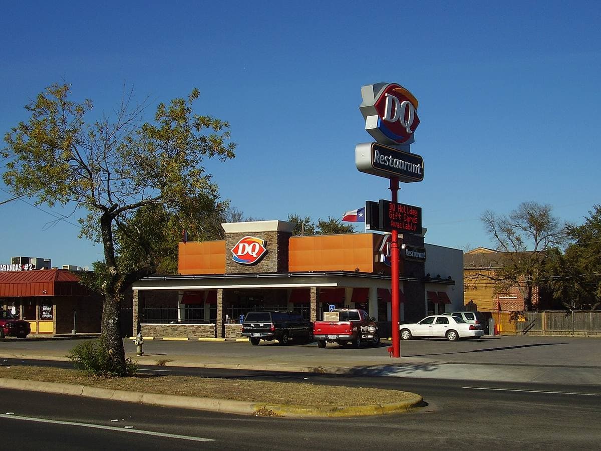 A Dairy Queen restaurant with its red roadside sign on a pole, under a deep blue sky