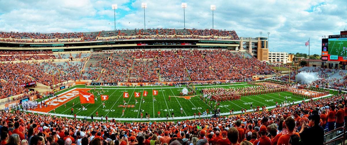 A panoramic view of a vast stadium packed with fans in burnt orange around a green field