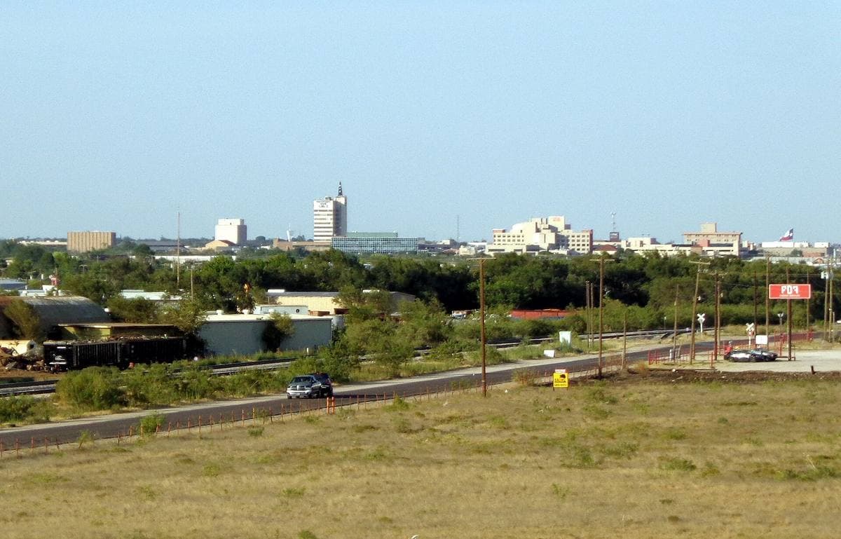 A flat West Texas city skyline beyond scrubland and a highway