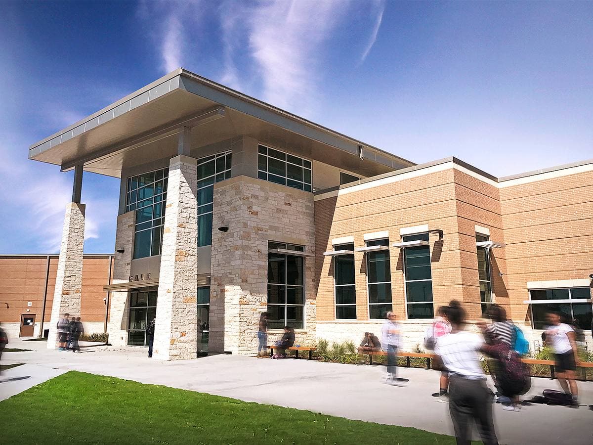 A modern brick and glass school entrance with students walking past on a sunny day