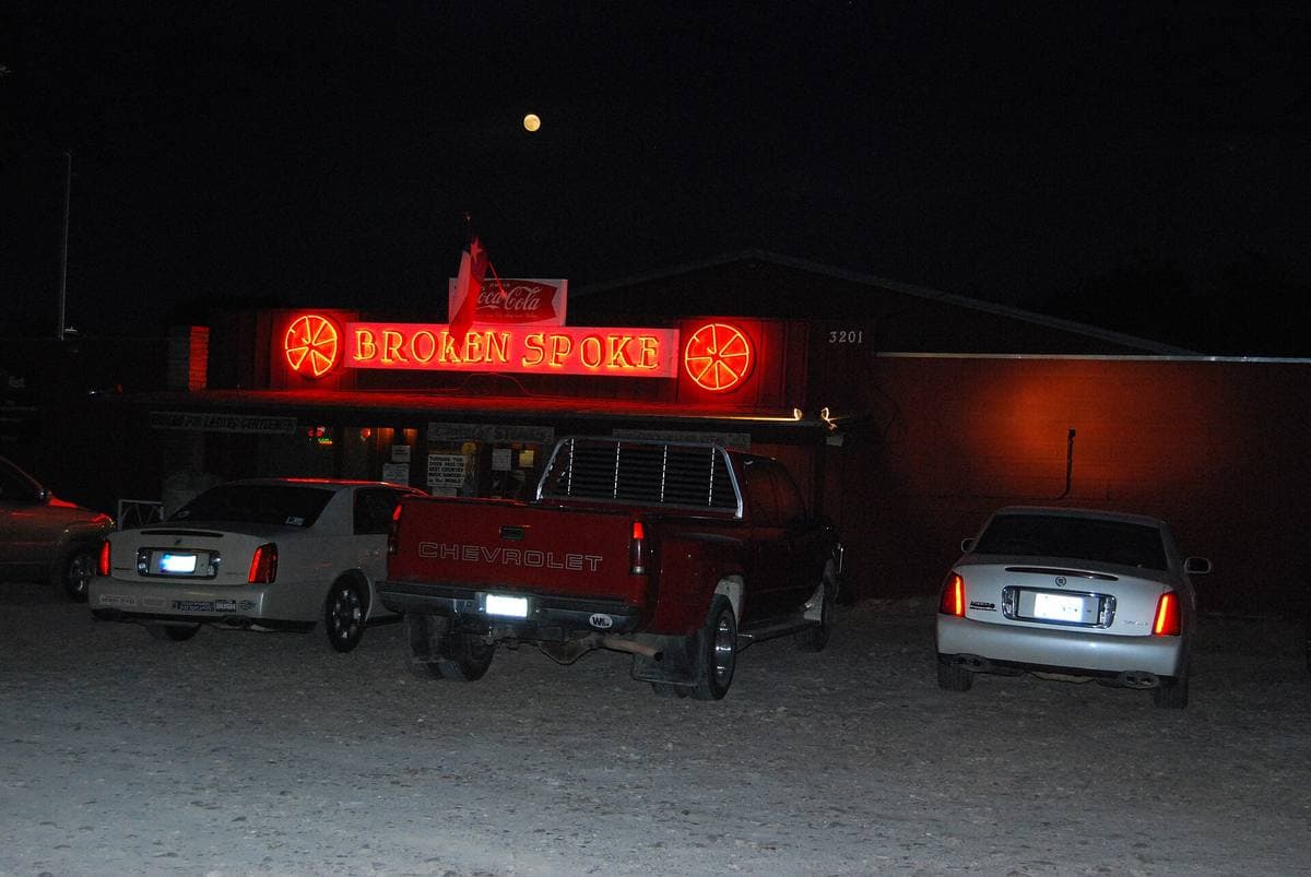 The Broken Spoke’s neon sign glowing red over pickups parked in the dark
