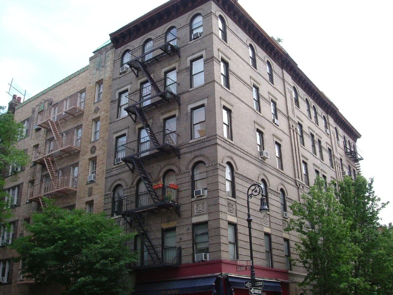 A six-storey brick corner building with black fire escapes, trees along Grove Street