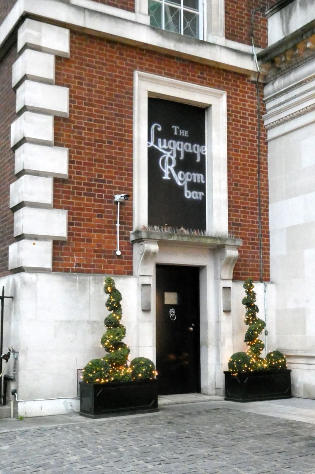 A dark-painted hotel front with a canopy and lamps on a Mayfair street corner