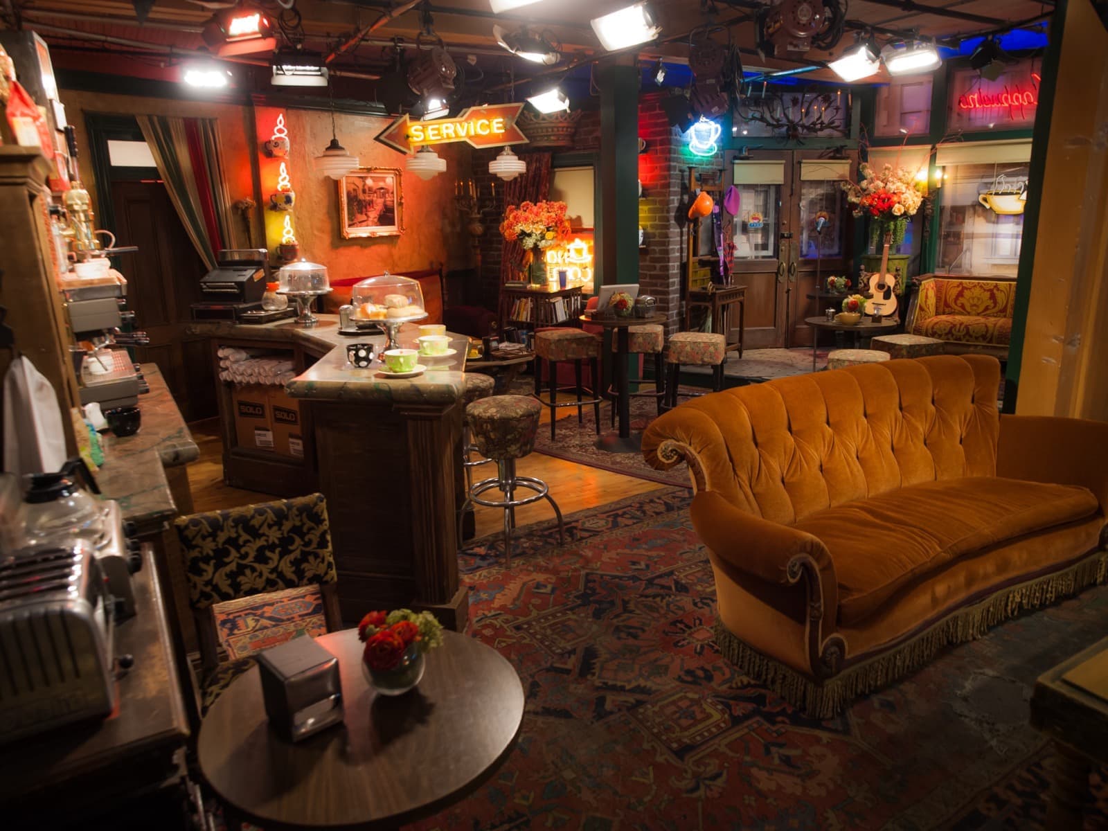 The café set with its orange sofa, armchairs, low table and brick walls under studio lights