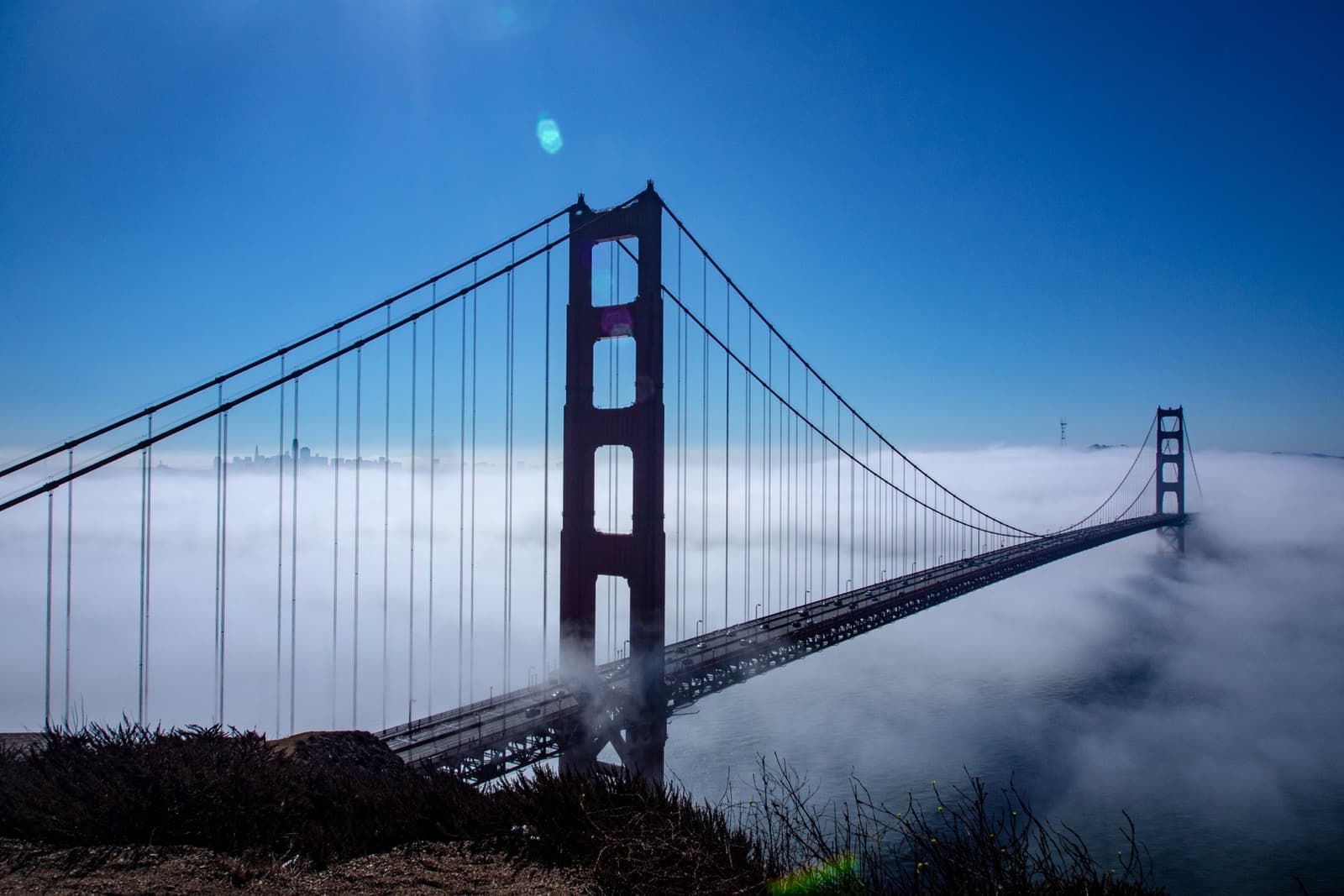 Both red towers of the Golden Gate Bridge rising out of a bank of white fog, the city beyond