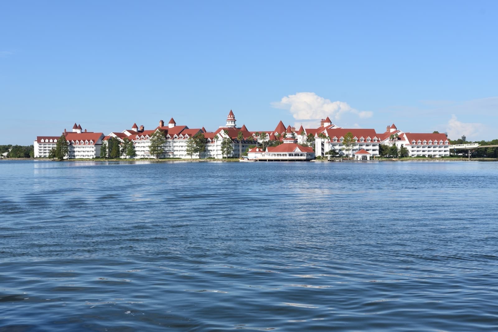 A long white Victorian-style hotel with red roofs across a wide blue lagoon