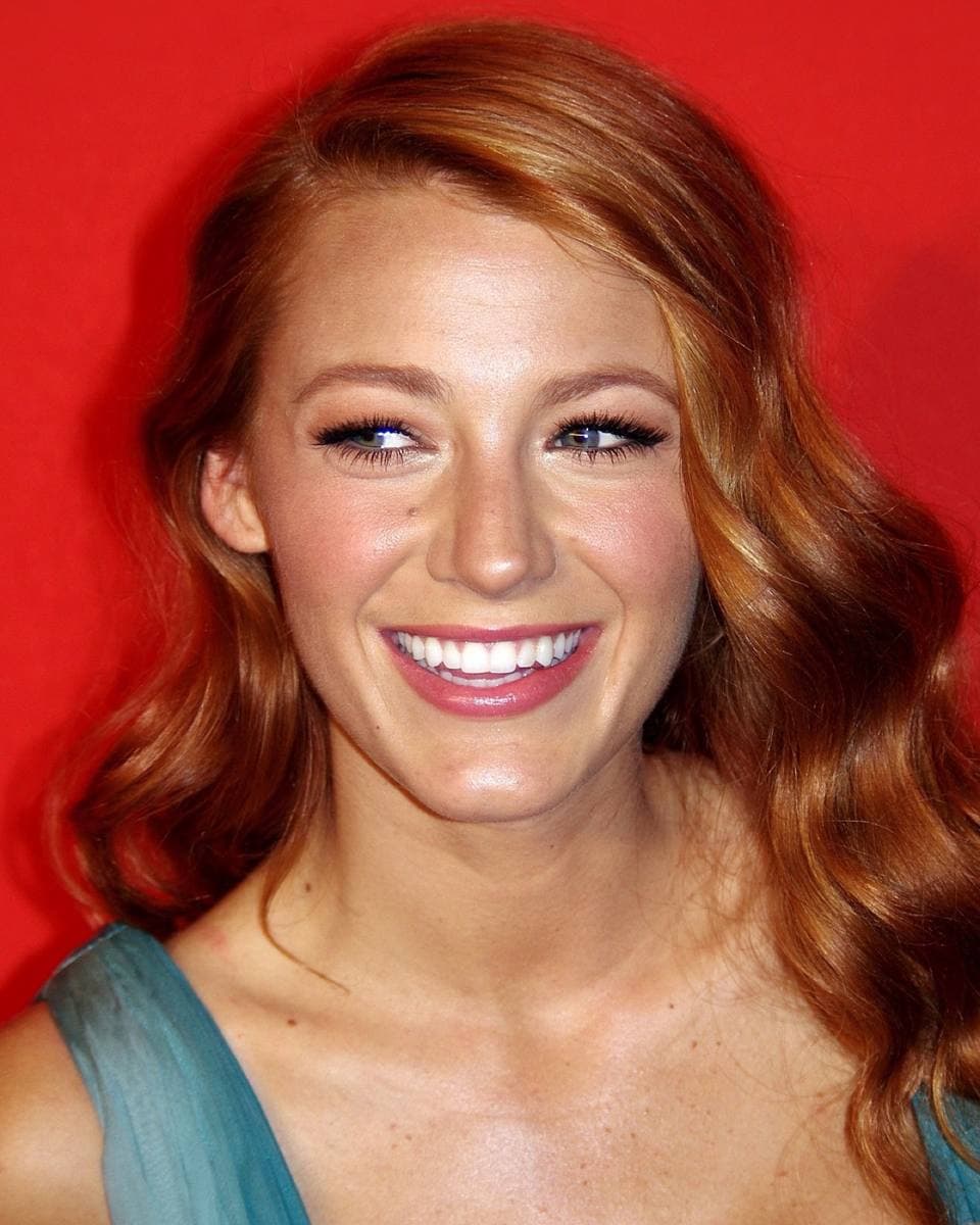 Blake Lively smiling, red hair loose, against a red backdrop