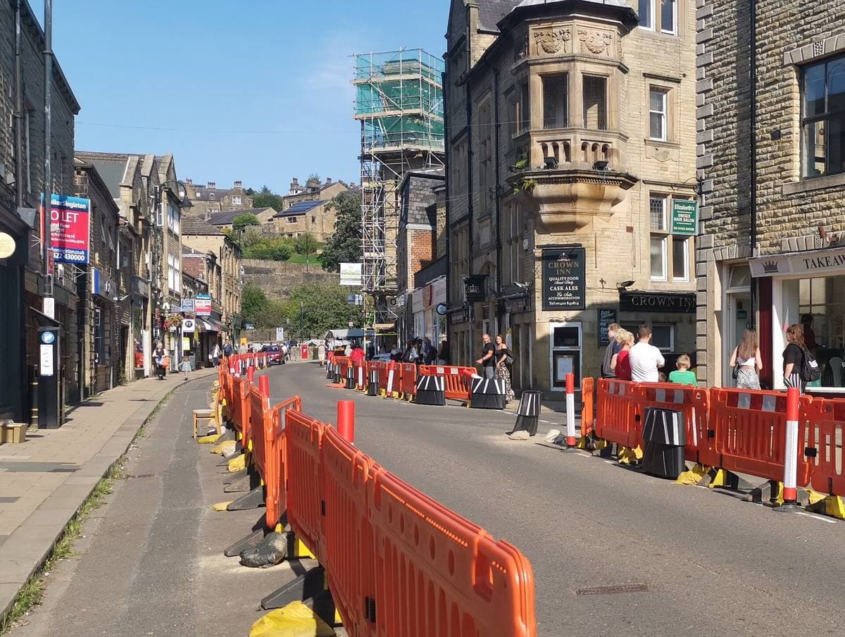 A busy stone-built shopping street with orange barriers along the kerb