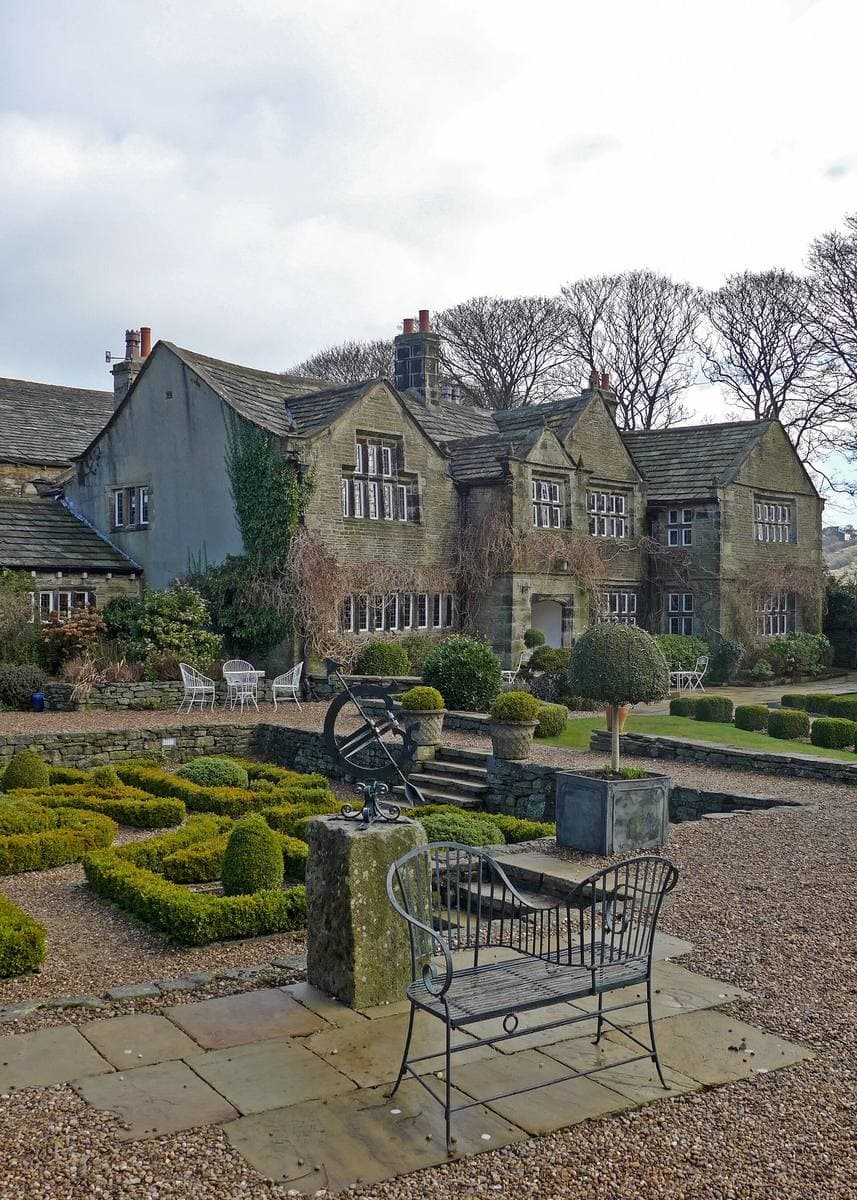 A grey stone gabled manor house behind a knot garden and a sundial
