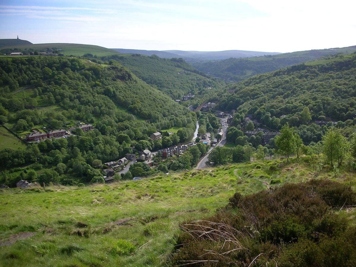 A steep wooded V of a valley with a town tucked into the bottom and moorland tops above