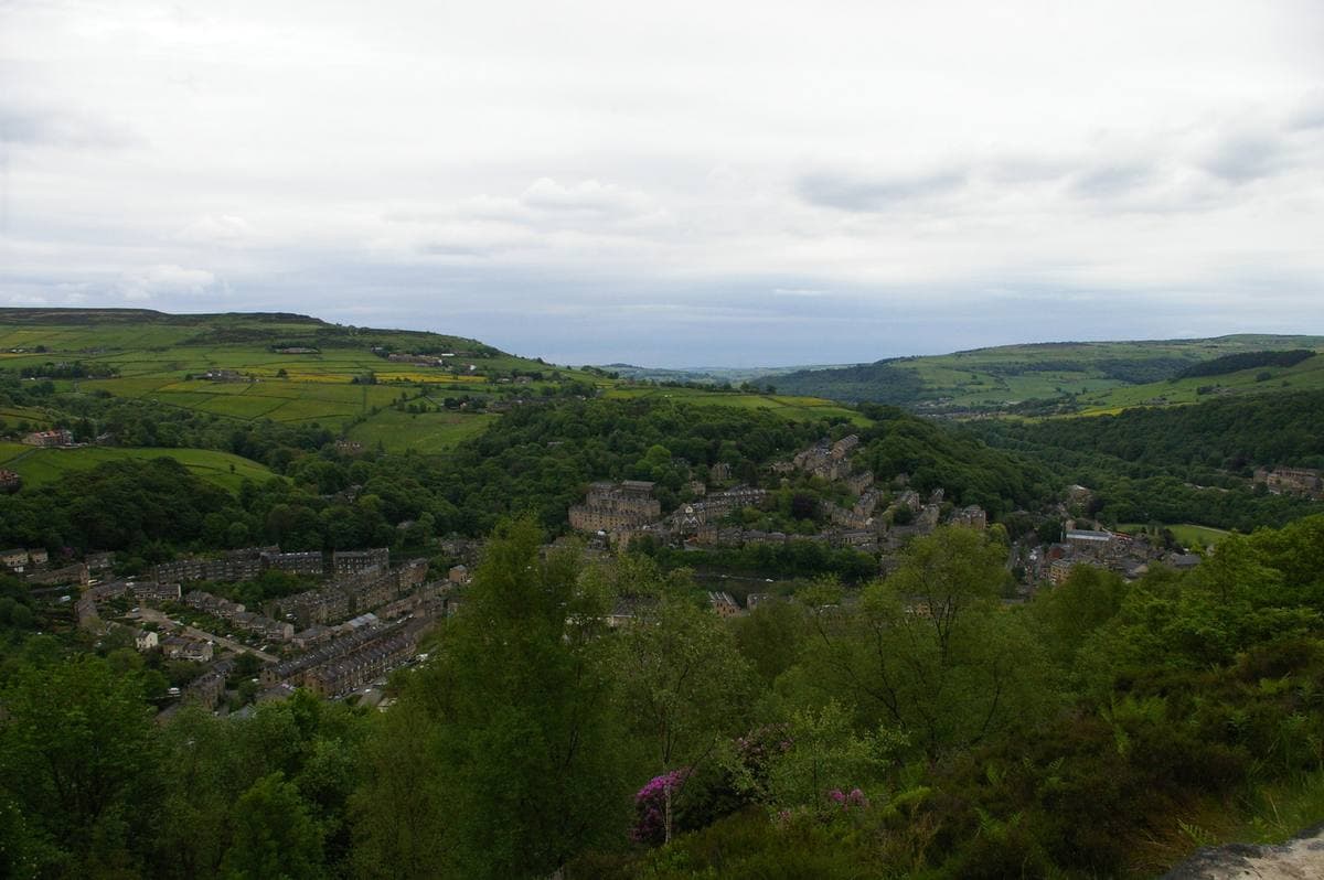 Rows of stone houses down a green valley side, with moorland across the valley