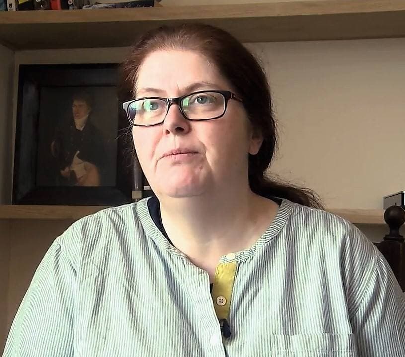 Sally Wainwright in glasses and a striped shirt, in front of a bookcase with a portrait