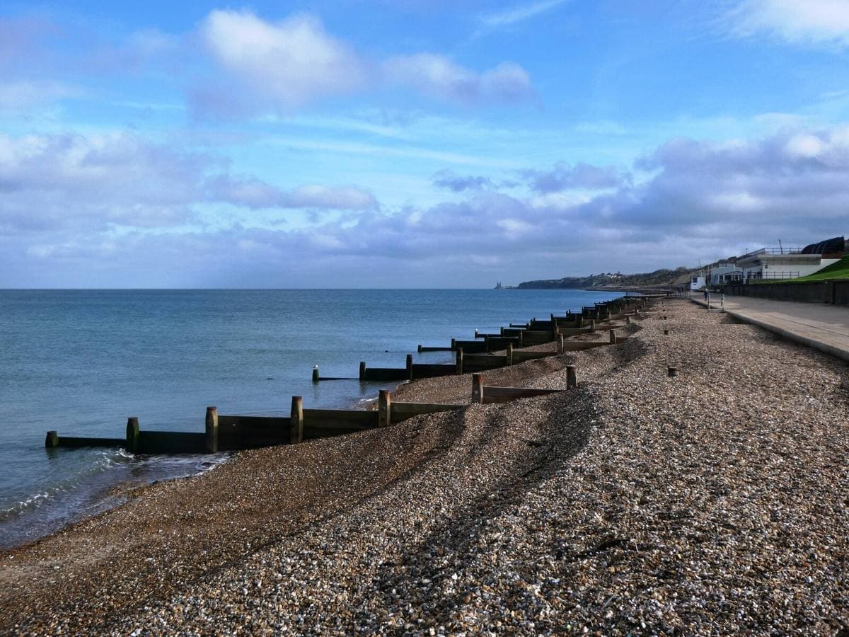 A shingle beach with wooden groynes running into a calm grey sea