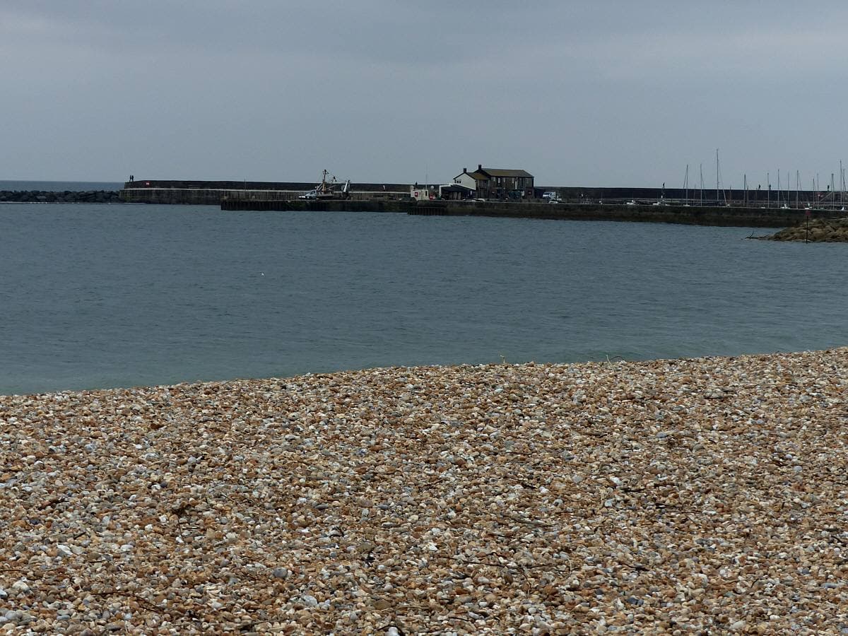 A sandy beach curving round to a stone harbour wall