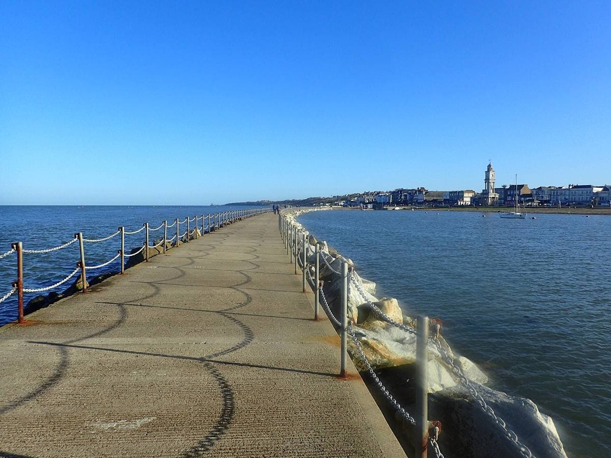 A long stone breakwater curving out into the sea under a pale sky