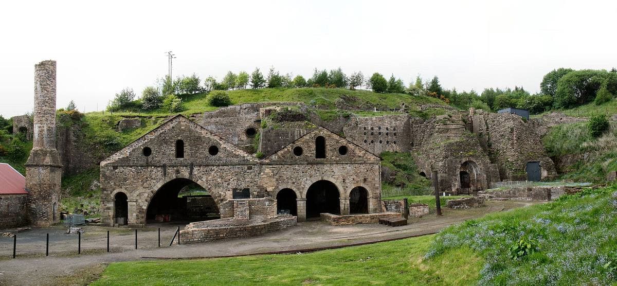 Ruined stone furnace buildings against a hillside