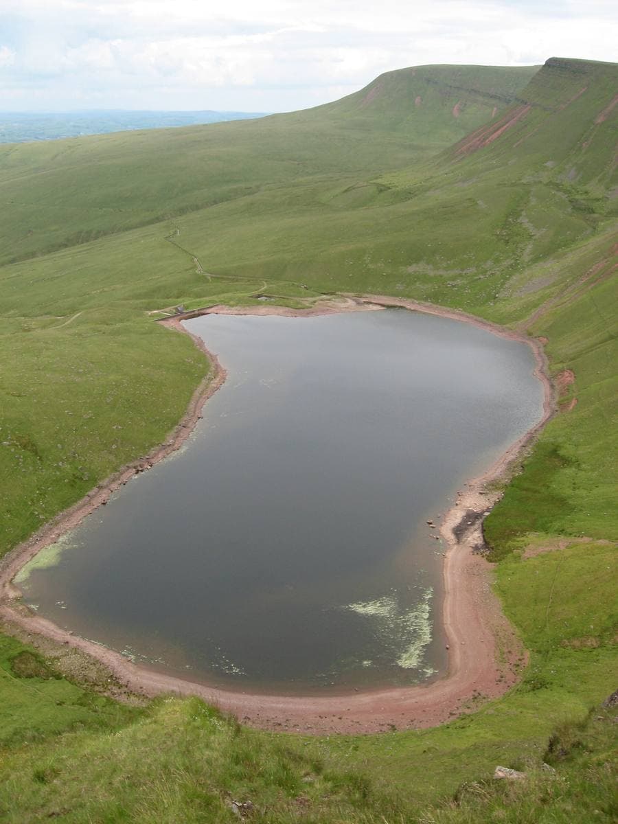 A dark lake far below a steep green escarpment