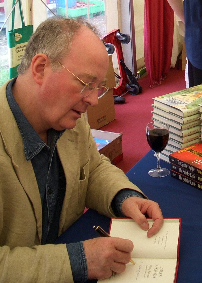 A grey-haired man in glasses signing a book at a table