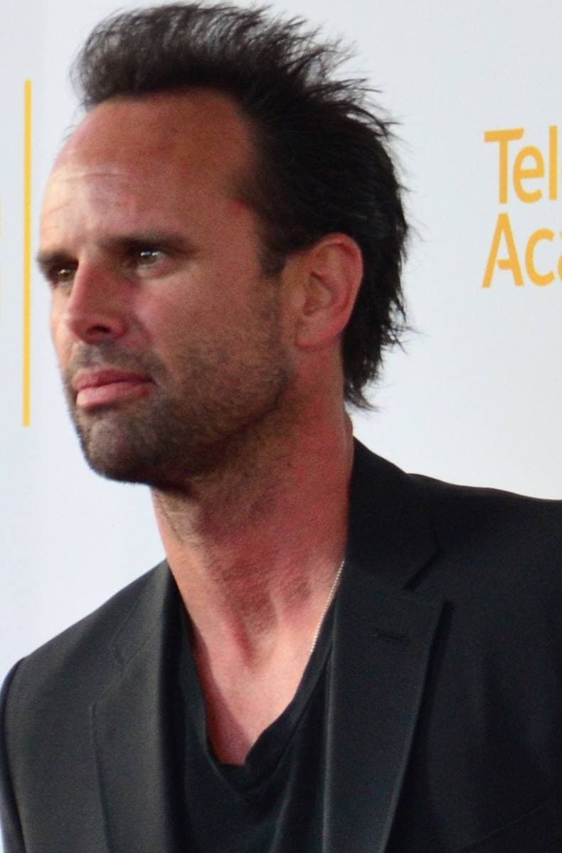 A man with a shaved head and a short beard in a dark suit