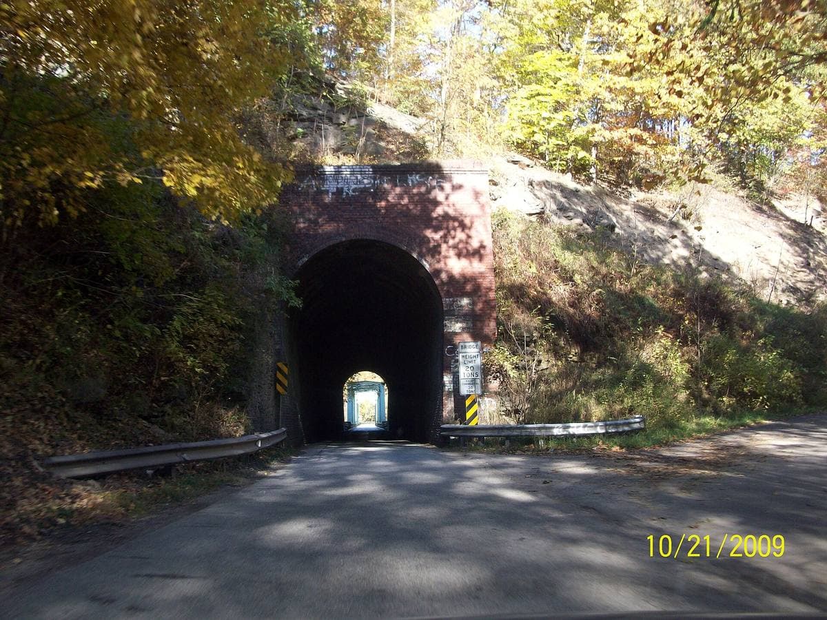 A narrow road running into a short stone tunnel under a railway