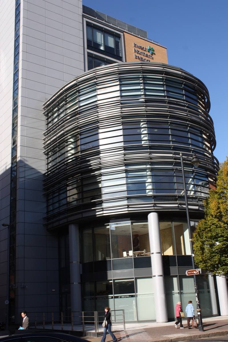 A rounded glass-and-steel corner tower with horizontal fins above a glazed ground floor on a city street