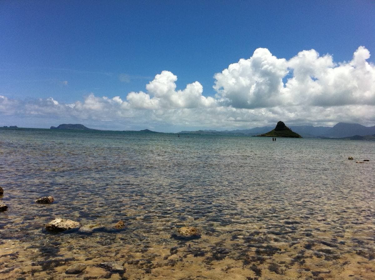 Clear shallow water over stones, a cone-shaped islet on the horizon under big clouds