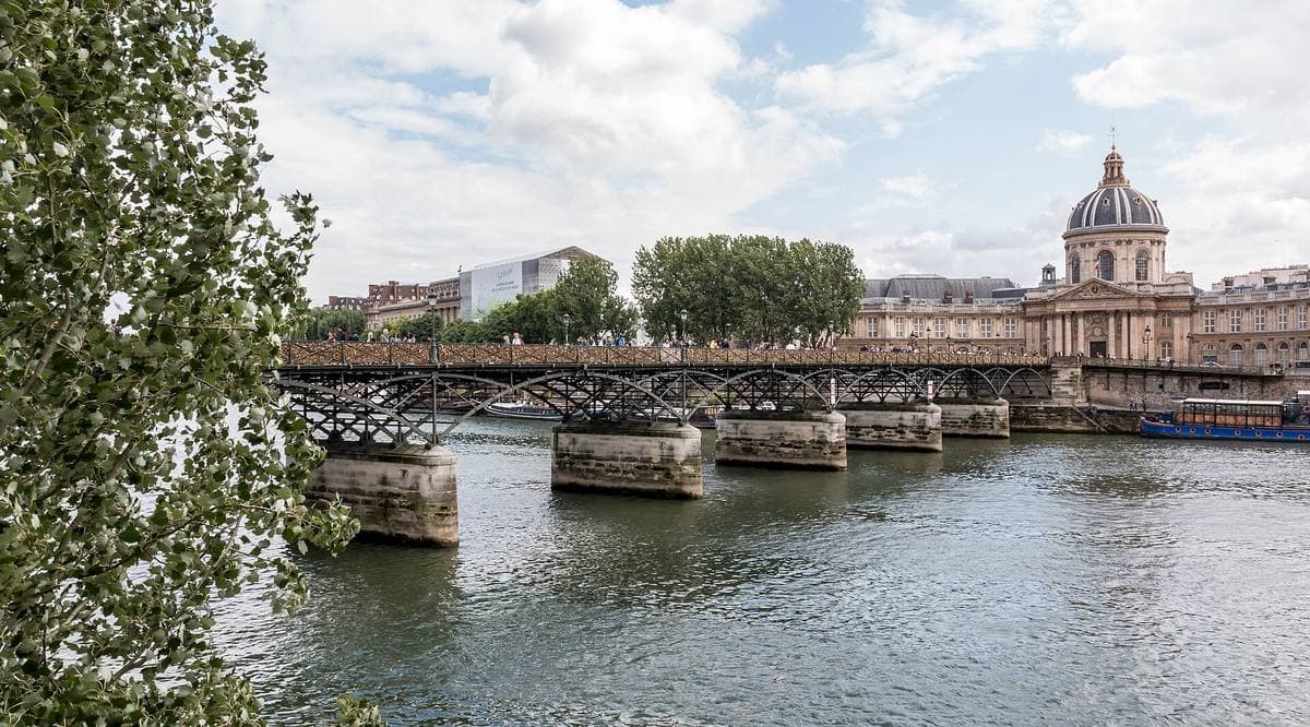 A low iron footbridge over the Seine leading to a domed building