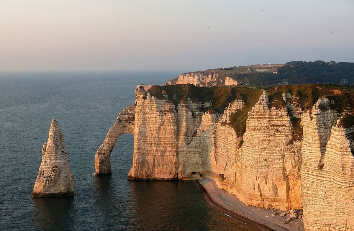 A white chalk needle and an arch of cliff glowing in evening light above the sea