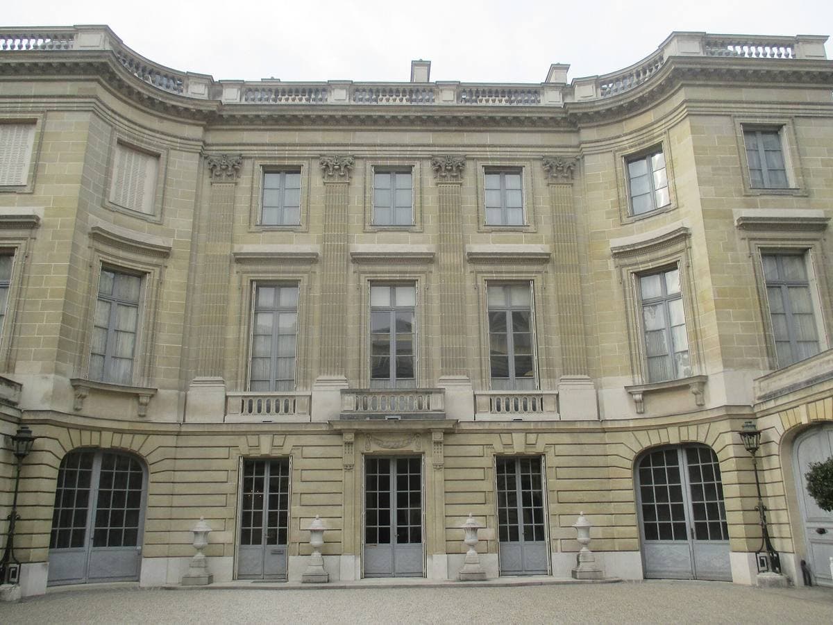 A curved pale stone mansion façade around a gravel courtyard