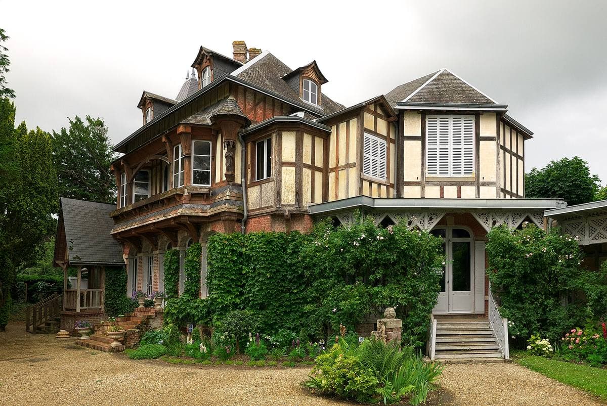 A half-timbered villa with balconies and ivy behind a gravel drive