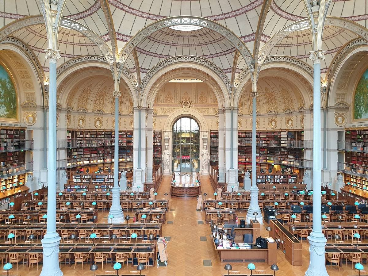 A reading room of slender iron columns, domes and painted lunettes over rows of desks