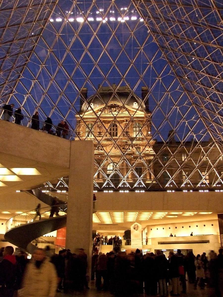 The diamond lattice of the Louvre pyramid seen from inside, with the palace beyond
