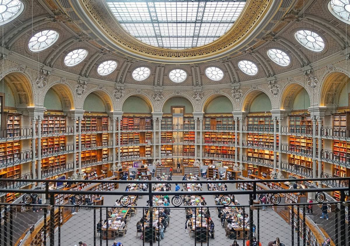 An oval reading room ringed with books under a glass roof and round windows