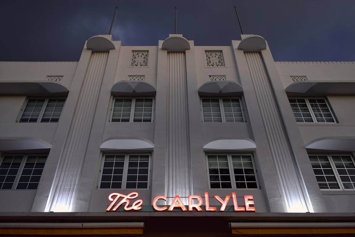 The white Art Deco front of the Carlyle at dusk with its neon name sign