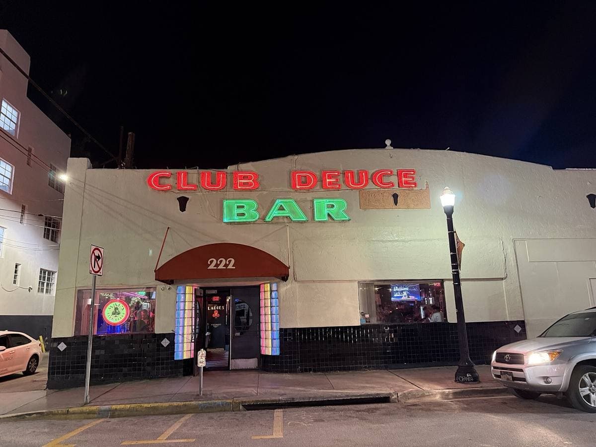A low corner bar at night with red and green neon reading Club Deuce Bar