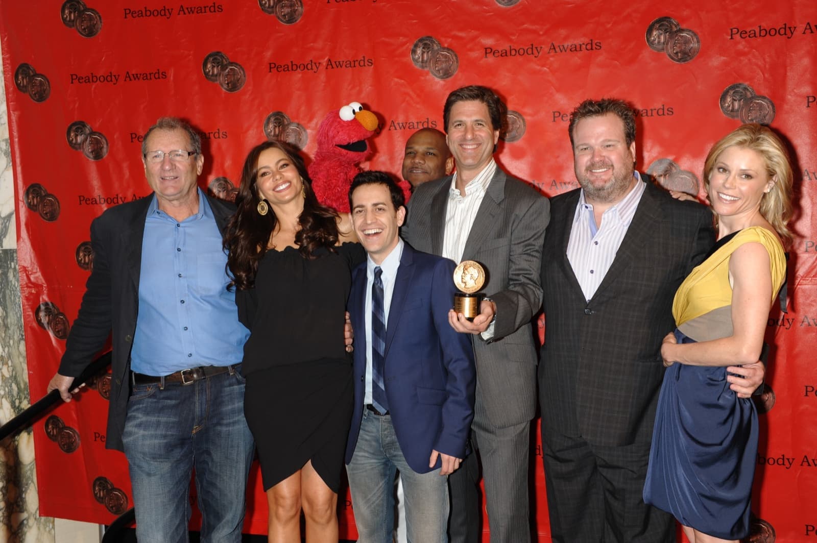 The Modern Family cast and producers in a row in front of a red Peabody Awards backdrop