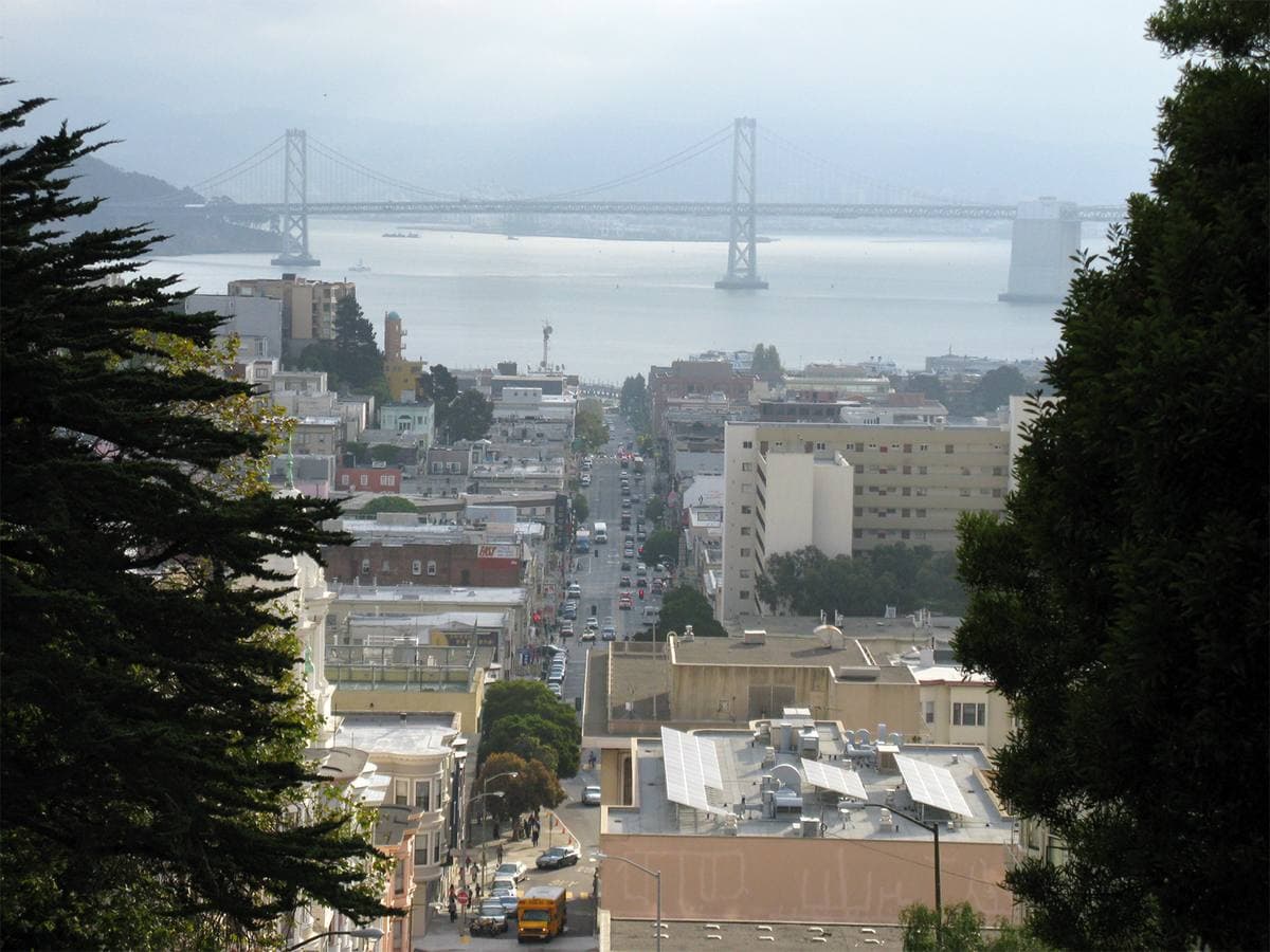 A steep street dropping between buildings to the bay and the Bay Bridge