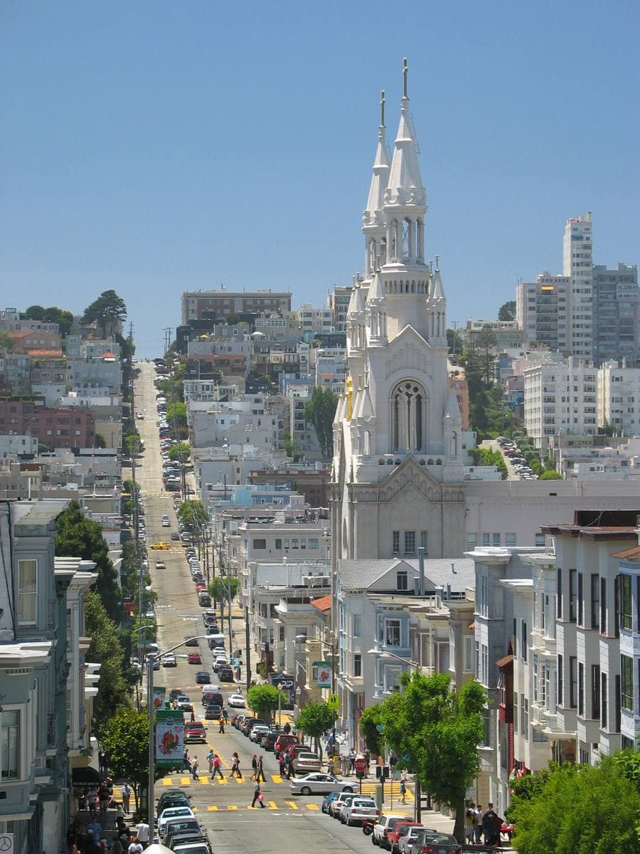 A city street rising past a white twin-spired church