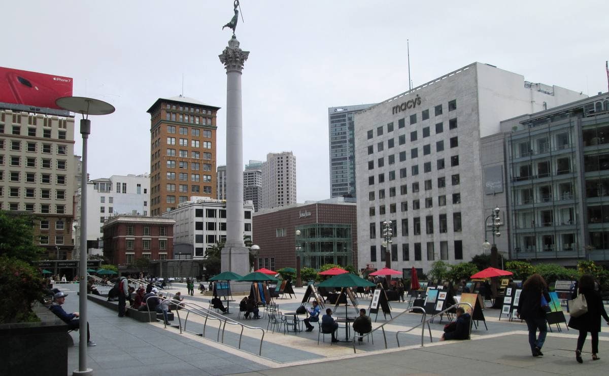 A paved city square with tables and a tall column topped by a statue