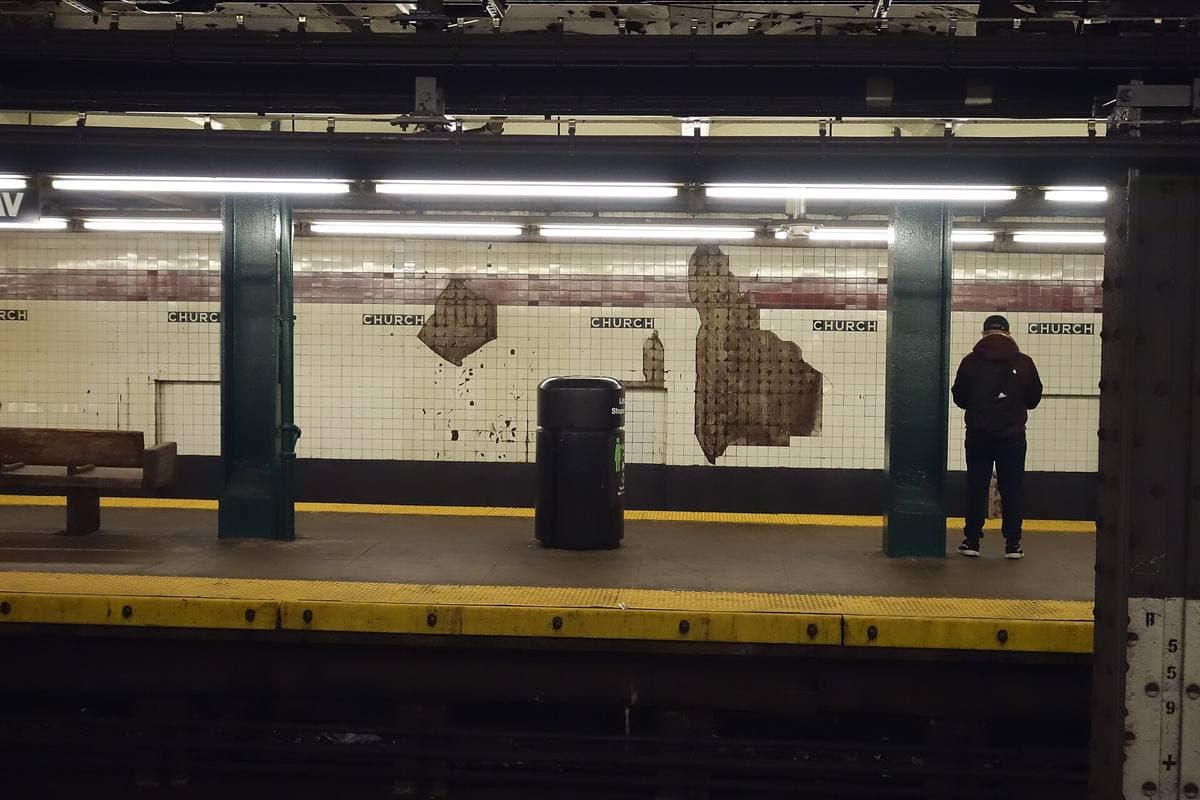 A subway platform with tiled walls reading Church, a man waiting