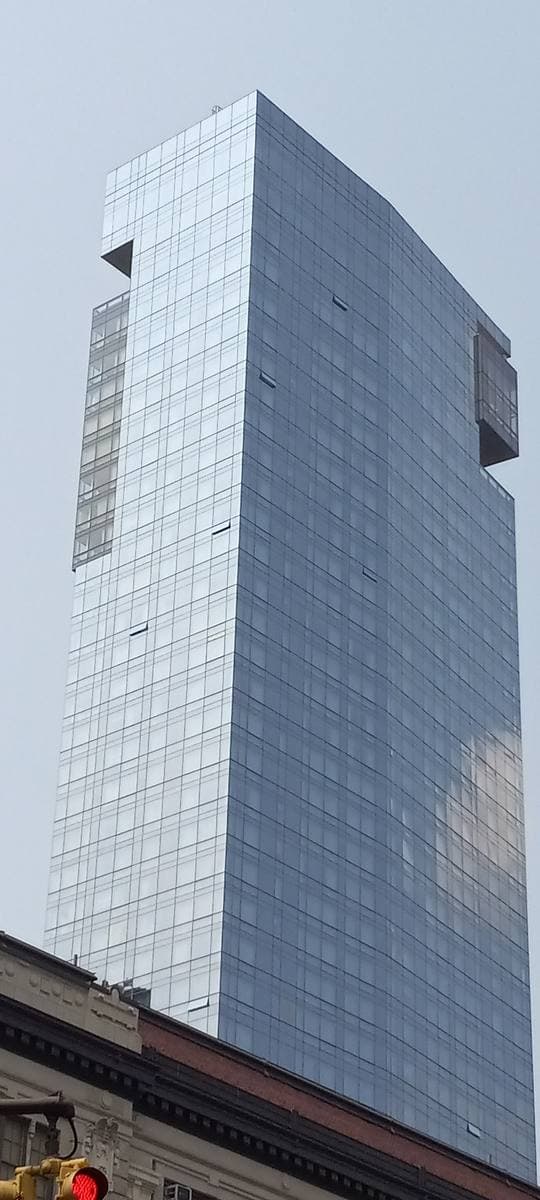 A tall glass hotel tower rising over low SoHo buildings