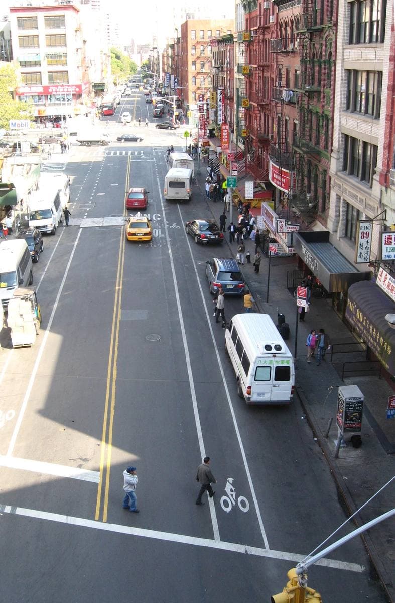 A long Lower East Side street seen from above, shopfronts and traffic